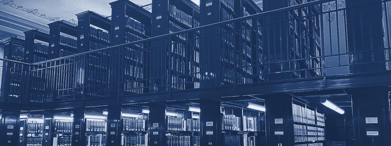 Two storeys of dark wooden stacks in a law library, filled with bound law reports, with a reading table and chairs in the foreground